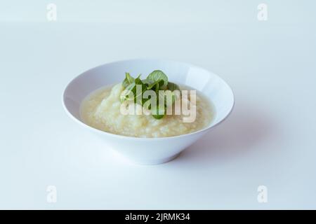 Gesunde vegane Blumenkohlcremesuppe mit Kräutern in weißer Schüssel auf weißem Tisch, Nahaufnahme Stockfoto