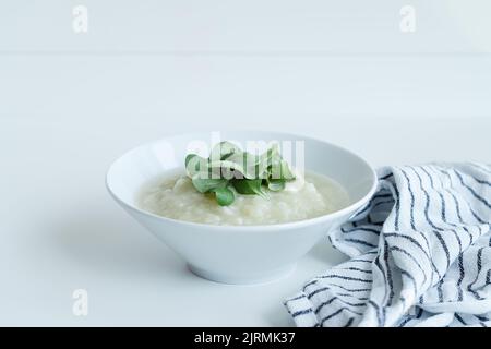 Gesunde vegane Blumenkohlcremesuppe mit Kräutern in weißer Schüssel auf weißem Tisch, Nahaufnahme Stockfoto