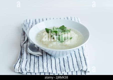 Gesunde vegane Blumenkohlcremesuppe mit Kräutern in weißer Schüssel auf weißem Tisch, Nahaufnahme Stockfoto