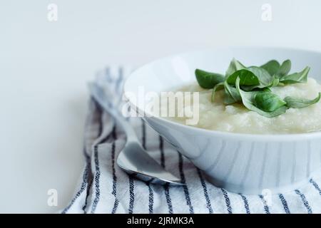 Gesunde vegane Blumenkohlcremesuppe mit Kräutern in weißer Schüssel auf weißem Tisch, Nahaufnahme Stockfoto