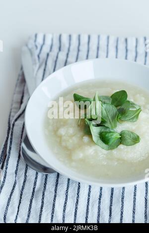 Gesunde vegane Blumenkohlcremesuppe mit Kräutern in weißer Schüssel auf weißem Tisch, Nahaufnahme Stockfoto