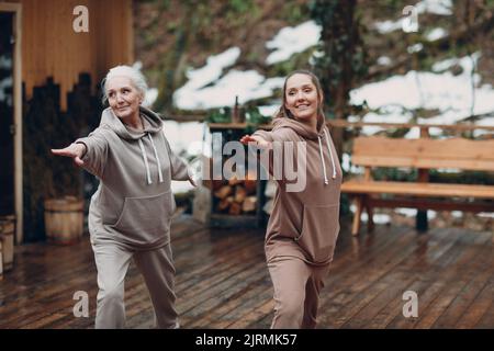 Frauen, die Sport und Fitness im Freien ausüben. Junge und ältere ältere Frauen wärmen sich auf und Yoga beim Glamping. Mutter und Tochter haben Zen wie einen modernen Fitnessurlaub Stockfoto
