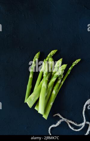 Roher biologischer grüner Spargel bereit zum Kochen auf dunklem Hintergrund, Draufsicht, Kopierraum. Pflanzliche Lebensmittel Stockfoto