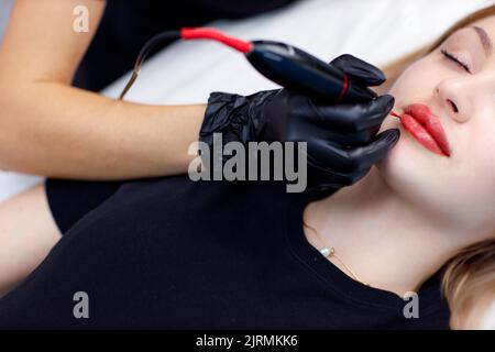 Kosmetologe Anwendung rosa Pigment Permanent Tattoo auf weibliche Lippen mit Tätowierung Nadel Maschine Stockfoto