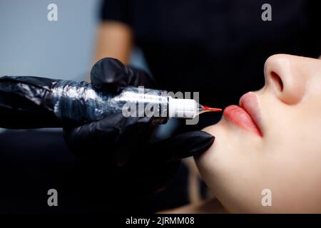 Kosmetologe, der rote dauerhafte Make-up-Tätowierung auf die Lippen einer jungen Frau anwendet. Stockfoto