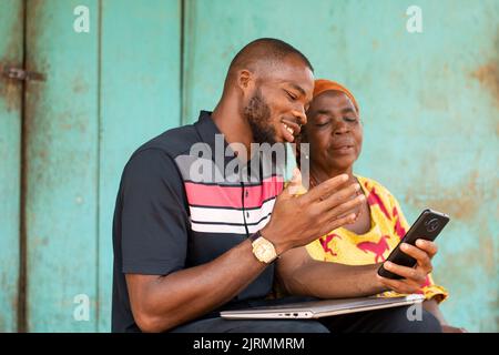 Ein junger schwarzer Mann zeigt eine alte afrikanische Frau auf seinem Telefon Stockfoto