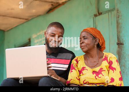Junger afrikanischer Mann, der mit einer älteren afrikanischen Frau über einen Laptop spricht Stockfoto