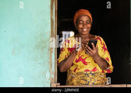 Glückliche ältere afrikanische Frau, die ihr Telefon benutzt Stockfoto
