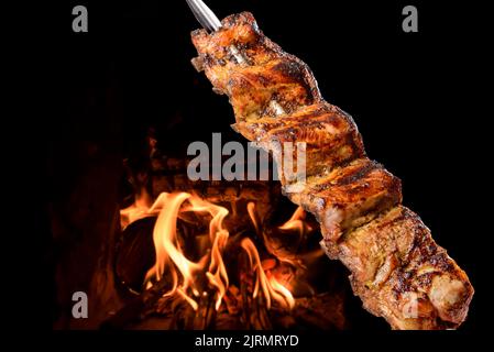 Grillen Sie Schweineribs auf Spiessen mit Feuer im Hintergrund. Brasilianische Küche. Stockfoto