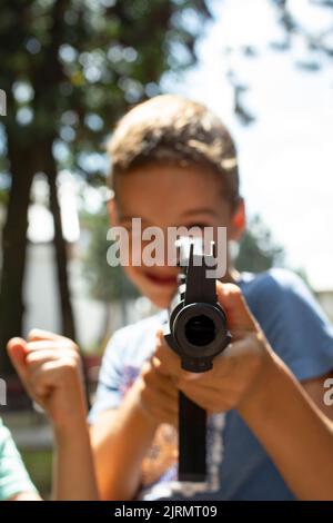 Defokussierte Kinder, die mit einem Gewehr auf die Kamera zeigen, draußen in einem Park, Aufnahmen mit weichem Fokus Stockfoto