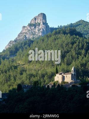 Am frühen Morgen trifft Sonnenlicht auf die Kirche von St-Benoit-en-Diois im französischen Drome-Departement. Oben erhebt sich die Felsformation, die als l'Aiguille bekannt ist Stockfoto