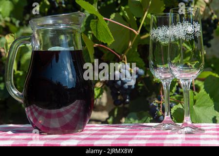 Glaskrug mit Rotwein und ein paar leere Weingläser auf dem Tisch. Stockfoto