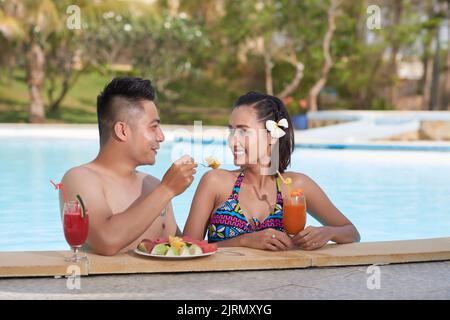 Schönes asiatisches Paar in der Liebe genießen frisches Obst und Getränke im Schwimmbad Stockfoto