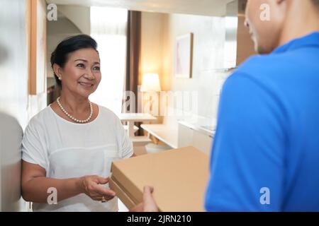 Fröhliche ältere vietnamesische Frau, die zu Hause Pizza bekommt Stockfoto