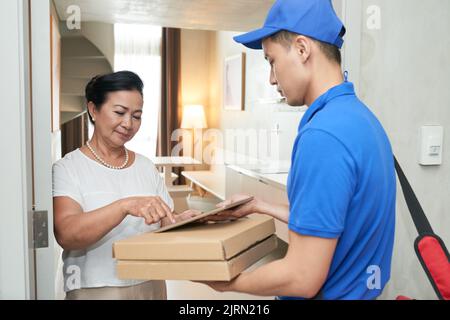 Kurier gibt älteren Frau Tablet zu unterzeichnen Dokument Stockfoto