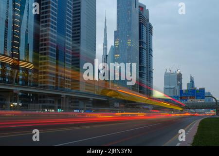 Gebäude und rasende Autos entlang der Sheikh Zayed Road, der längsten Autobahn in Dubai und den Vereinigten Arabischen Emiraten. Stadtbild im Freien bei Dämmerung. Stockfoto