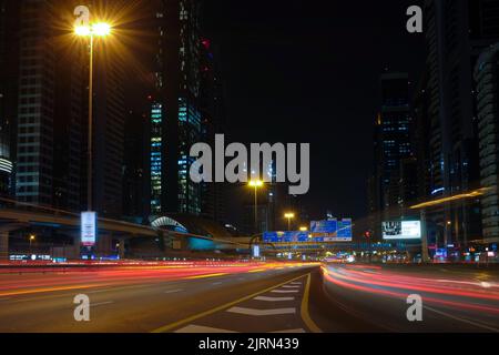 Hohe Gebäude und schnelle Autos entlang der Sheikh Zayed Road, der längsten Autobahn in Dubai und den Vereinigten Arabischen Emiraten. Nachts Stadtbild im Freien. Stockfoto