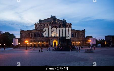 Dresden, Deutschland-August 17,2022:Menschen sitzen nach Sonnenuntergang unter einer Statue vor der Semperoper. Stockfoto