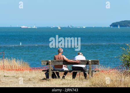 Rückansicht eines älteren Paares, das auf einer Bank sitzt und an einem Sommertag den Blick über den Solent im Lepe Country Park, Hampshire England, genießt Stockfoto