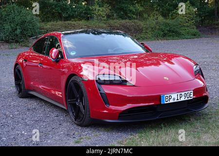 Rheine, NRW, Deutschland - August 24 2022 Ein roter Porsche Taycan parkte auf Schotter. Dies ist eine elektrische Limousine und die erste serienmäßig produzierte elektrische Ca Stockfoto