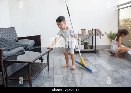 Lustige junge Kind Reinigung Boden zu Hause. Junge Waschboden mit Wischstock auf dem Balkon der modernen Wohnung. Männlicher Haushalt hilft ordentlich Haus. Kinder helfen gerne bei der Hausreinigung. Stockfoto