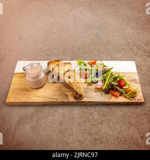 Köstliche Entenleber-Pastete in einem Glas serviert mit geröstetem Brot und Salat Stockfoto