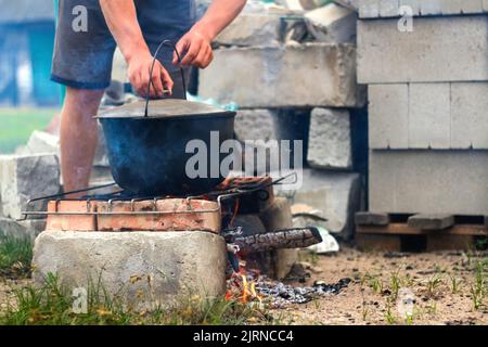 Unschärfe-Mann Kochen Fischsuppe im Eisen Bowler über einem Lagerfeuer. Fischsuppe kocht im Kessel auf dem Scheiterhaufen. Suppe in einem Topf im Feuer. Camp am Tag. Entfällt Stockfoto