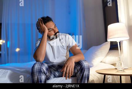 Gestresster indischer Mann, der nachts auf dem Bett saß Stockfoto