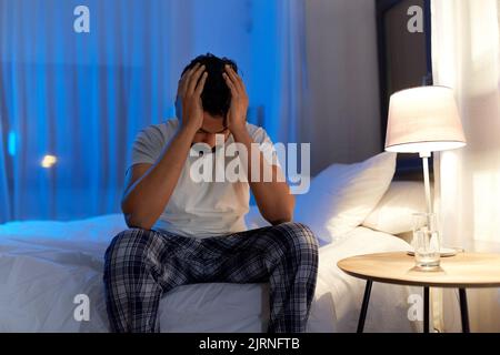 Gestresster indischer Mann, der nachts auf dem Bett saß Stockfoto