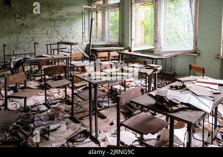 Zerfallen und vandalisiert Klassenzimmer in Prypiat. Schreibtische und Sitze stehen noch, aber viele Bücher sind auf dem Boden verteilt.Tschernobyl-Sperrzone Stockfoto