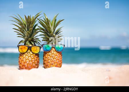 Ananas in stylischer Sonnenbrille auf dem Sand gegen Meer Stockfoto