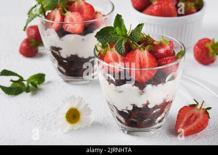 Kleinigkeiten. Brownies, frische Erdbeere und Mascarpone-Creme in Schichten auf Glas auf weißem Hintergrund gezackt. Portionsdesserts. Kein gebackener Brownie Cheesecak Stockfoto