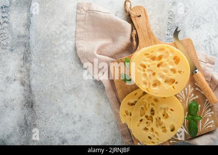 Käse Maasdam oder Radamer. Stück Käse auf Holzstanda auf altem grauen Betonhintergrund. Draufsicht. Freier Speicherplatz für Ihren Text. Stockfoto