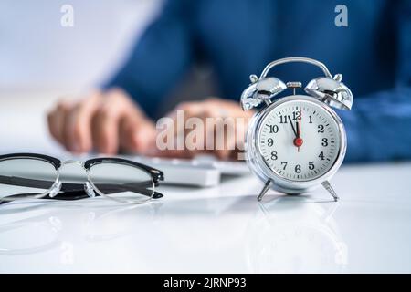 Ein Wecker Vor Dem Geschäftsmann, Der Am Arbeitsplatz Arbeitet Stockfoto
