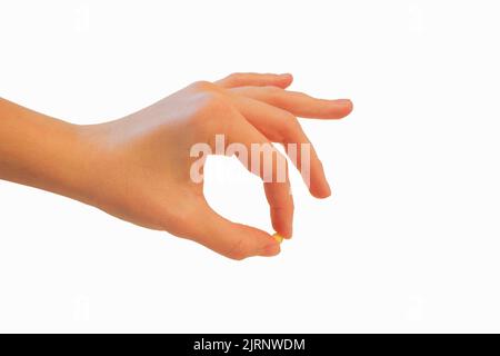 Die linke weibliche Hand, isoliert auf einem weißen Hintergrund, hält eine kleine gelbe Pillengeste. Stockfoto