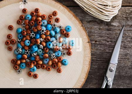 Ein Stapel aus Holz-Türkis und Metallbeern auf der Holzoberfläche mit Sissors und Kordel für die Schmuckherstellung. Blick von oben. Stockfoto