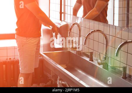 Handwaschbecken aus Edelstahl in einem modernen Gefängnis, Beleuchtung, Straffung. Der Gefangene trocknet seine Hände. Stockfoto