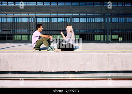 Ein glückliches Teenager-Paar sitzt am Bahnhof und macht Fotos. Stockfoto