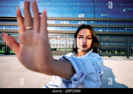 Ein fröhliches Teenager-Mädchen sitzt an einem sonnigen Tag im Freien am Bahnhof und spielt mit Schatten. Stockfoto