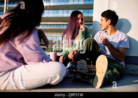 Eine kleine Gruppe von Teenagern, die draußen sitzen und Fast Food für einen Snack essen. Urbane Jugendliche hängen nach der Schule ab. Stockfoto
