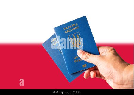 Zwei biometrische ukrainische Pässe in der Hand eines Mannes vor dem Hintergrund der polnischen Nationalflagge. Persönliche Identifikation, Freundschaft zwischen t Stockfoto