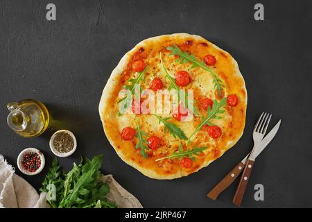 Traditionelle italienische Pizza mit Tomaten und Rugula auf dunklem Hintergrund - hausgemacht. Draufsicht, Copy Space. Stockfoto