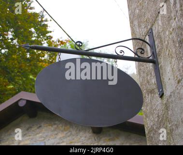 Ovales, dunkles Schild mit verzierten Ornamenten an einer Wand im mittelalterlichen Stil. Im Hintergrund können Sie den Himmel, die Vegetation und mehr alten Stil bauen sehen Stockfoto