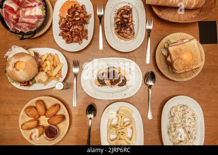 Teller und Tabletts mit typischen Rezepten der spanischen Gastronomie mit Croquette Tapas, gegrilltem Ohr, Alioli-Kartoffeln, Tintenfisch im andalusischen Stil, Toast und Broken Stockfoto