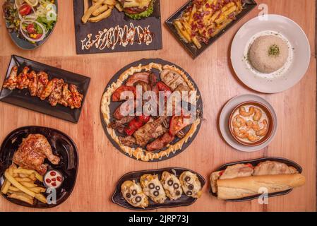 Set von Platten mit Lebensmitteln im Ofen mit einem zentralen Tablett mit verschiedenen Braten Fleisch, Holzkohle gegrilltes Huhn, Flügel mit Büffelsauce, Salate und po gekocht Stockfoto