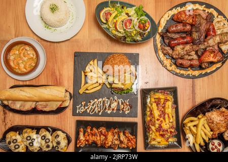 Set von Platten mit Lebensmitteln im Ofen mit einem zentralen Tablett mit verschiedenen Braten Fleisch, Holzkohle gegrilltes Huhn, Flügel mit Büffelsauce, Salate und po gekocht Stockfoto
