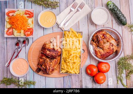 Set aus köstlichen, vom Holzkohlegrill gegrillten Hähnchengerichten für die Hauszustellung mit Obst-, Gurken- und Tomatensalaten und verschiedenen Saucen Stockfoto