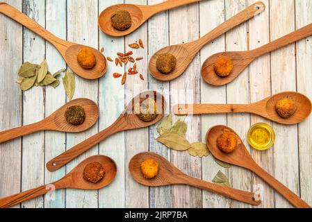 Set von köstlichen Kroketten in verschiedenen Geschmacksrichtungen und Texturen auf Holzlöffel mit Öl, Lorbeerblättern und Chilis Stockfoto