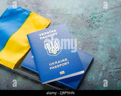 Zwei biometrische ukrainische Pässe und eine kleine Flagge der Ukraine auf dunklem Hintergrund. Persönliche Identifizierung, Reisen, Tourismus, Flucht aus dem Krieg in Ukrai Stockfoto