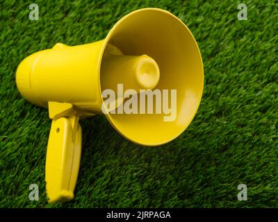 Nahaufnahme. Gelbes Megaphon auf einem grünen Rasen. Minimalismus. Gerüchte, Fälschungen, falsche Informationen. Kundgebungen, Demonstrationen, Debatten vor den Wahlen. Es gibt keine Stockfoto